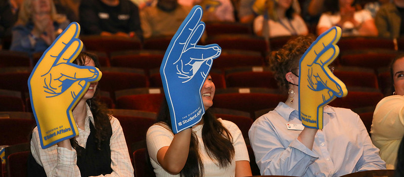 Employees waving their zot foam hands while seated inside the Barclay theatre.